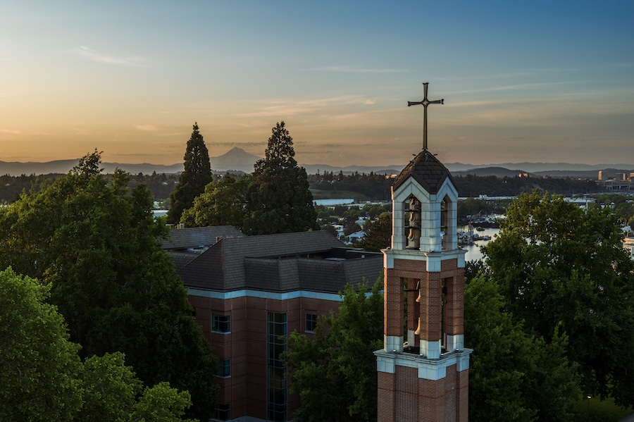 A drone captured image of the UP bell tower at eye level with the sunrise and Mt Hood visible in the background.