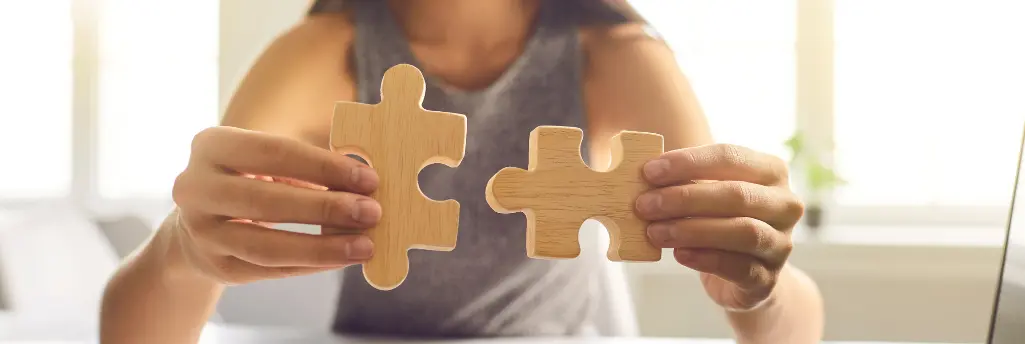 A person holding two wooden puzzle pieces that fit together, symbolizing problem-solving or teamwork.