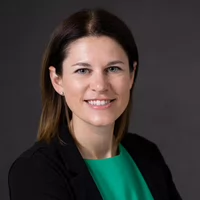 Professional headshot of a smiling woman in a green top and black blazer.