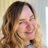 A smiling woman with wavy hair posed against a blurred background.