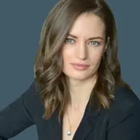 Professional headshot of a woman with shoulder-length wavy hair, wearing a black blazer and a subtle necklace.