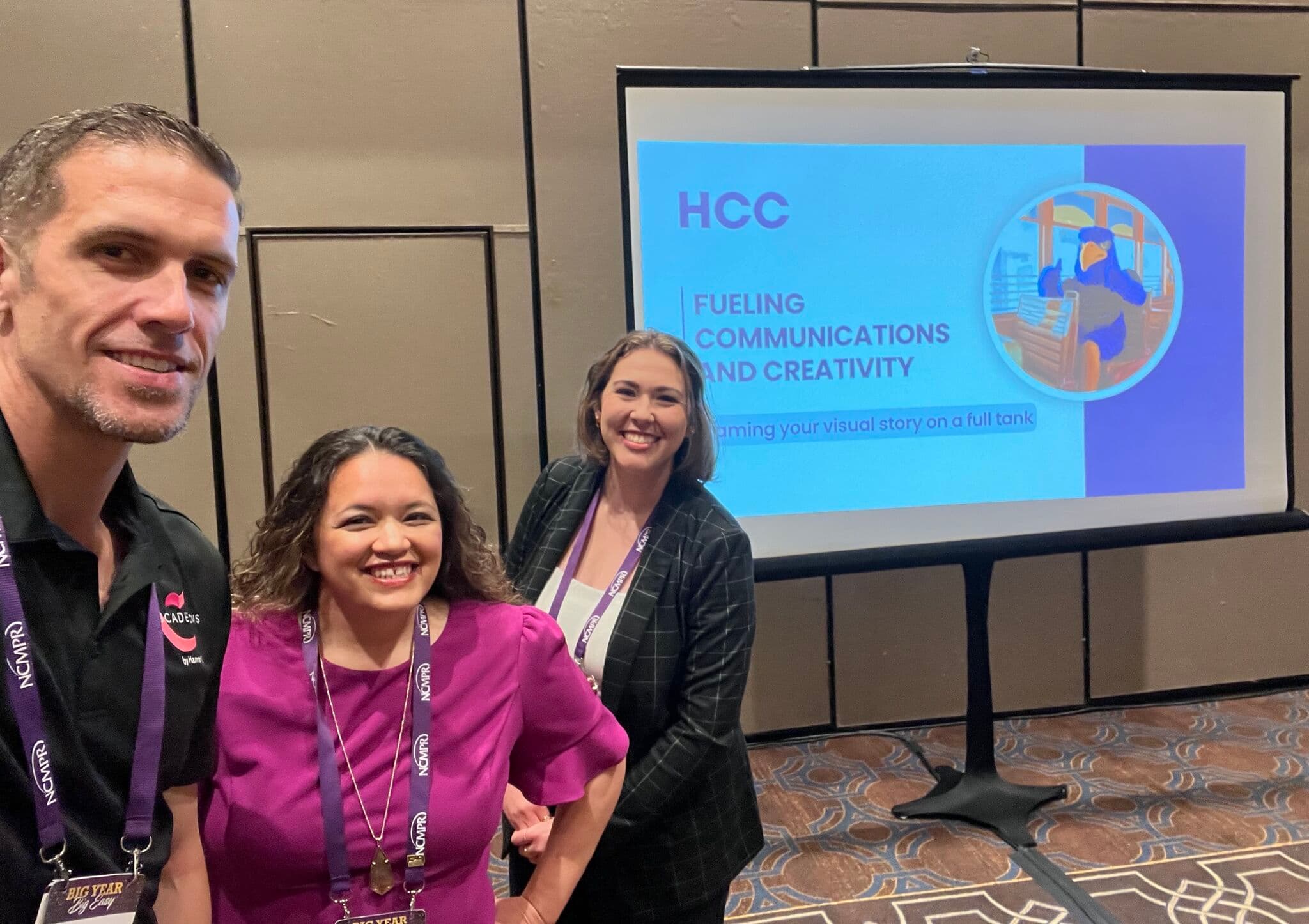 Three presenters smiling in front of a screen displaying the title "HCC: Fueling Communications and Creativity".