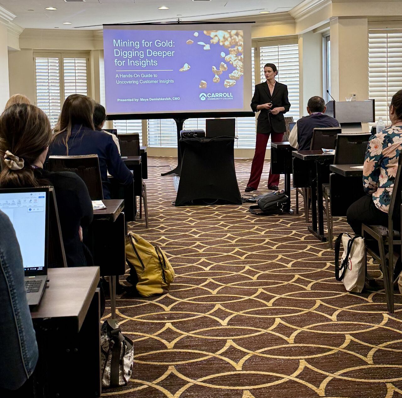 Speaker presenting a workshop titled "Mining for Gold: Digging Deeper for Insights" in a conference setting, with attendees seated and focused on the presentation.