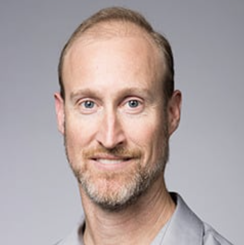 Headshot of a smiling man with a beard and light hair, wearing a gray shirt.