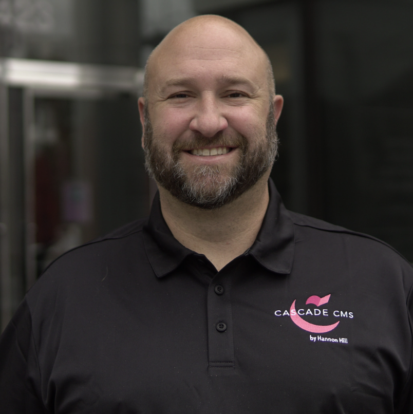 A smiling man wearing a black polo shirt with the "Cascade CMS" logo.